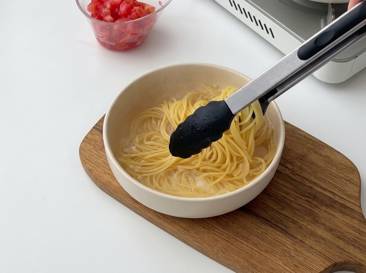 Pince noire transférant les spaghetti cuits de leau chaude vers un bol deau froide.