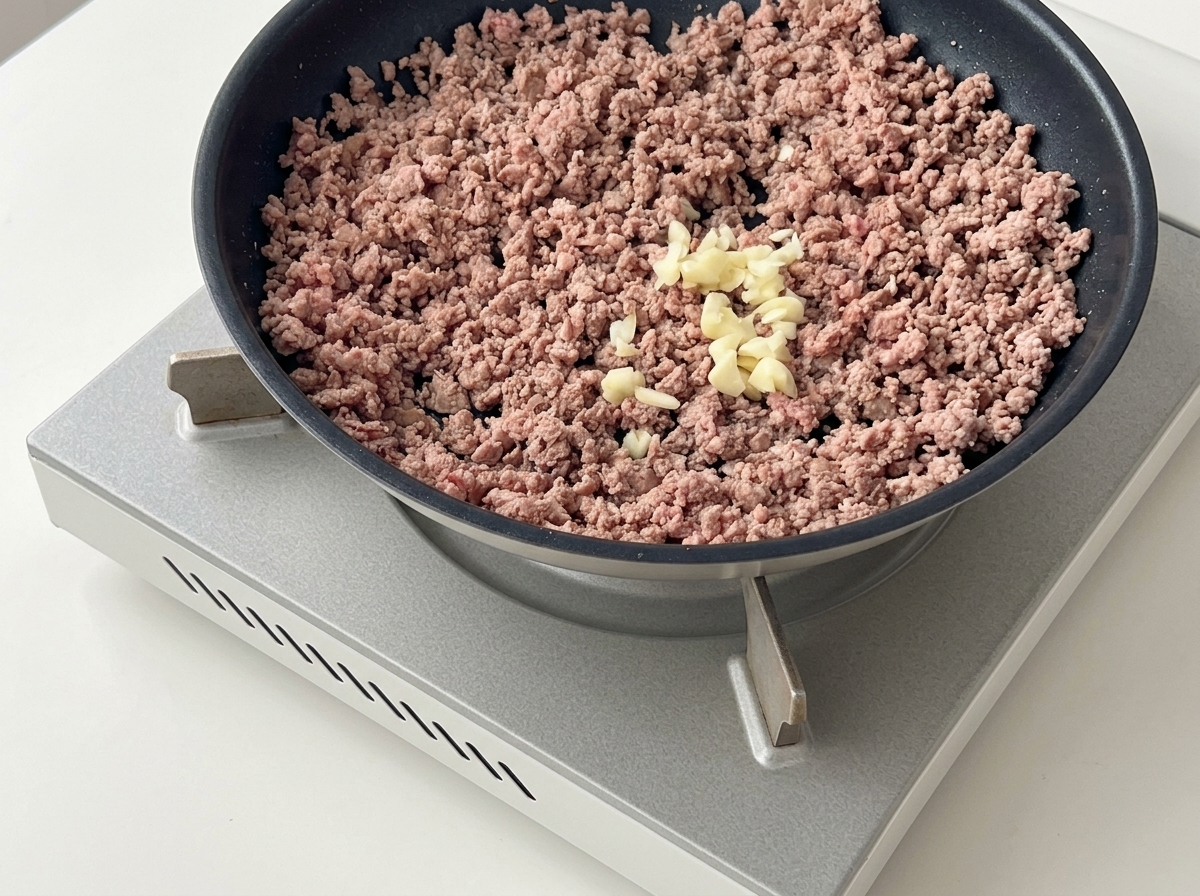 Ail haché ajouté sur le bœuf haché doré dans une poêle sombre.