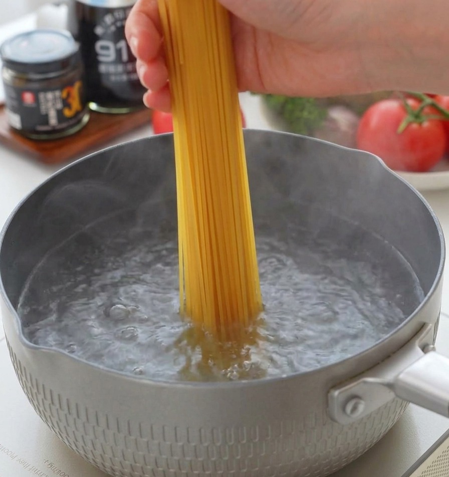 Une main plaçant des spaghettis secs verticalement dans une casserole deau bouillante.