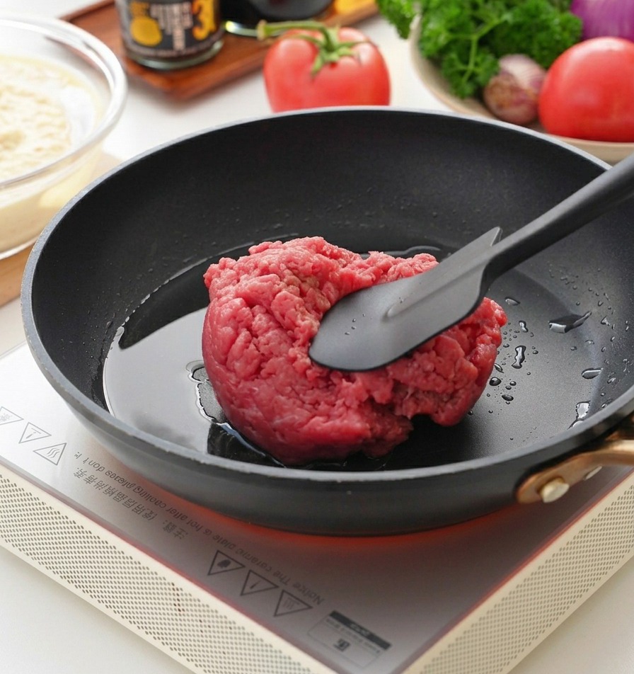 Une spatule pressant du bœuf haché cru dans une poêle chaude.