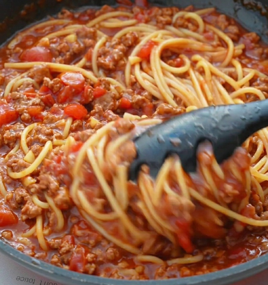Pince mélangeant les spaghettis dans la sauce tomate pour bien les enrober.