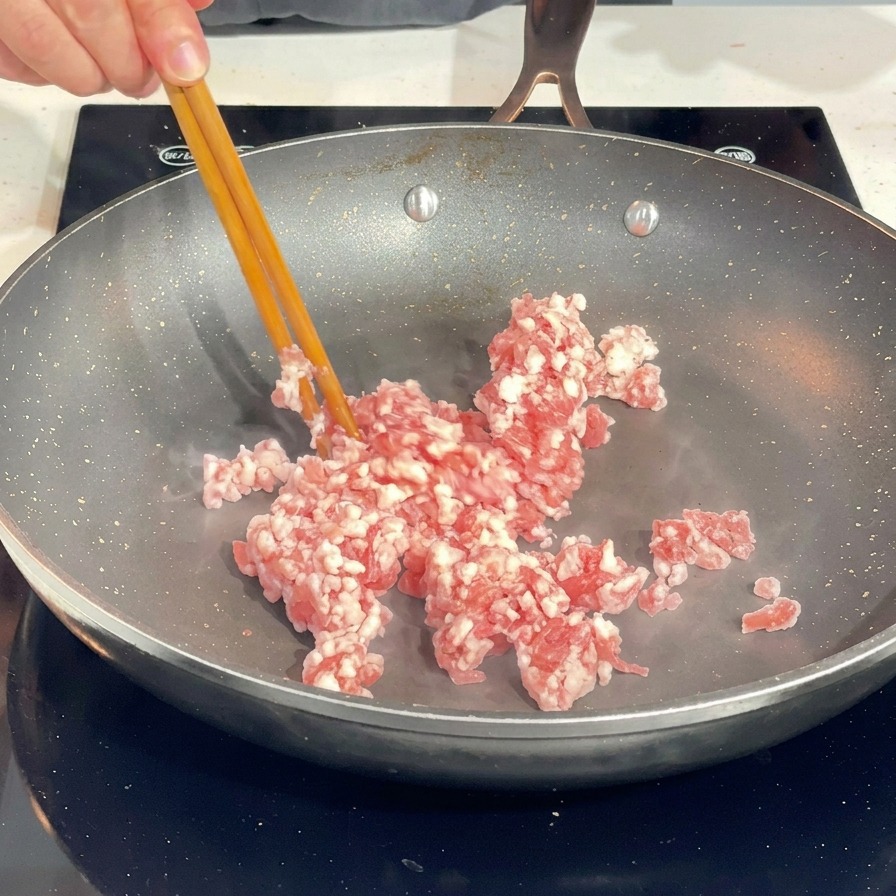 Utilisation de baguettes pour séparer la viande de porc hachée crue dans une poêle chaude.
