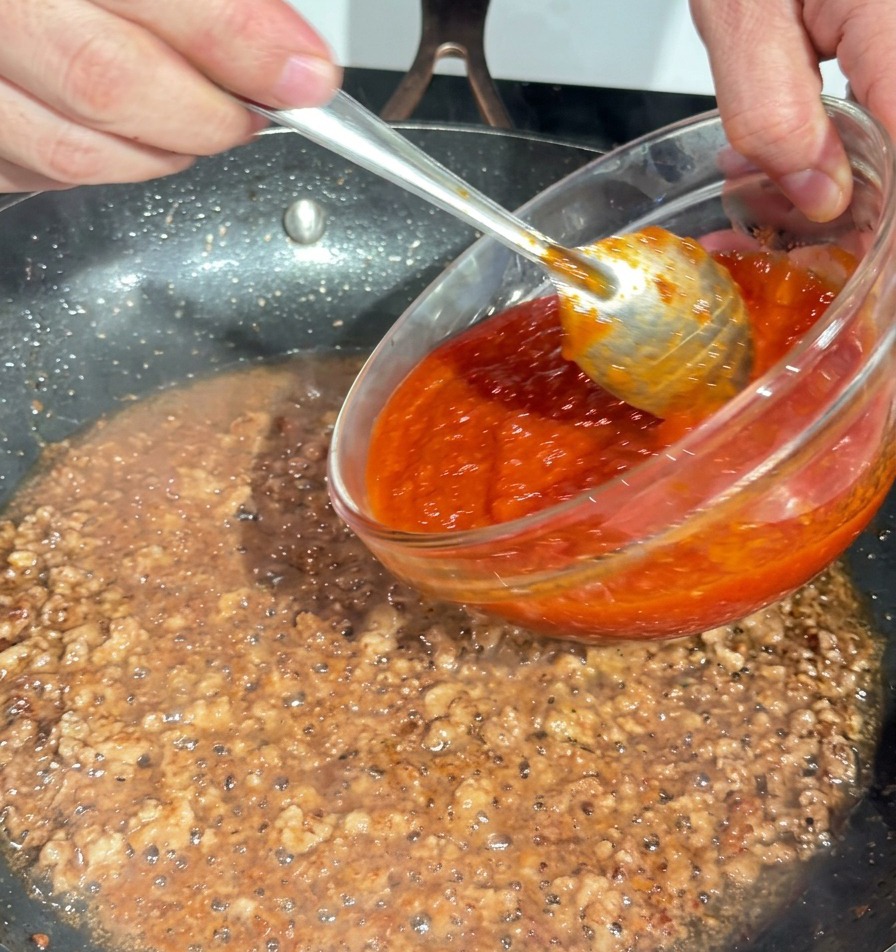 Verser une sauce tomate rouge épaisse dun bol en verre dans une poêle de porc haché doré.