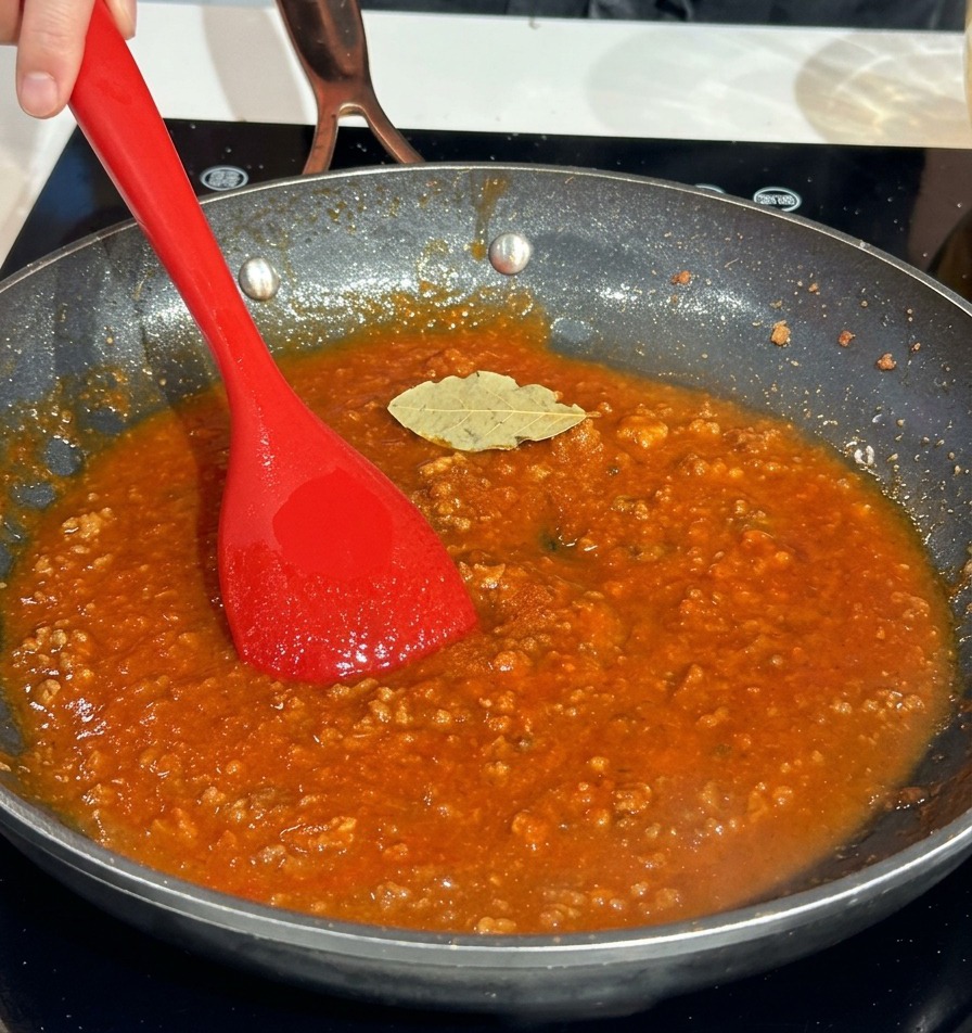 Une feuille de laurier séchée posée sur une riche sauce à la viande rouge dans une poêle.