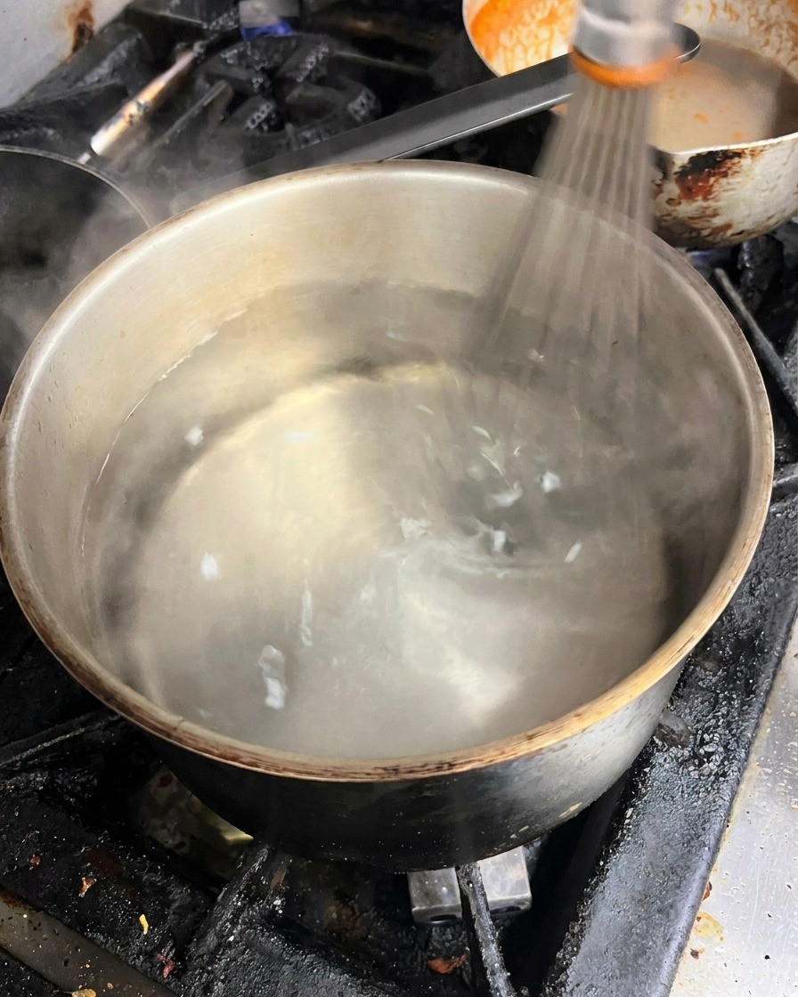 Un fouet mélangeant de leau frémissante dans une casserole pour créer un vortex central.