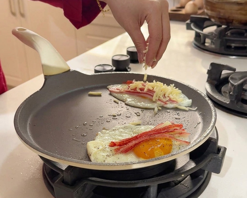 Une main saupoudrant du fromage râpé sur les œufs et le surimi en cuisson.