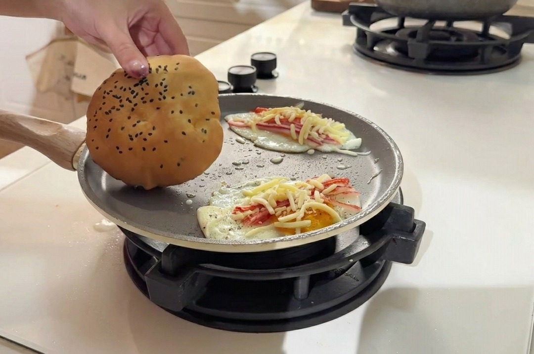 Pose dun pain burger aux graines de sésame sur la surface de la poêle à côté des galettes dœufs.