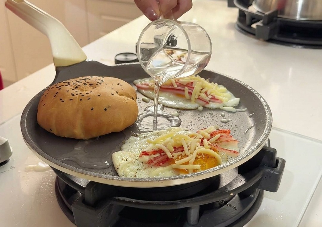 Versement deau claire depuis un petit verre dans la poêle chaude entre le pain et les œufs.