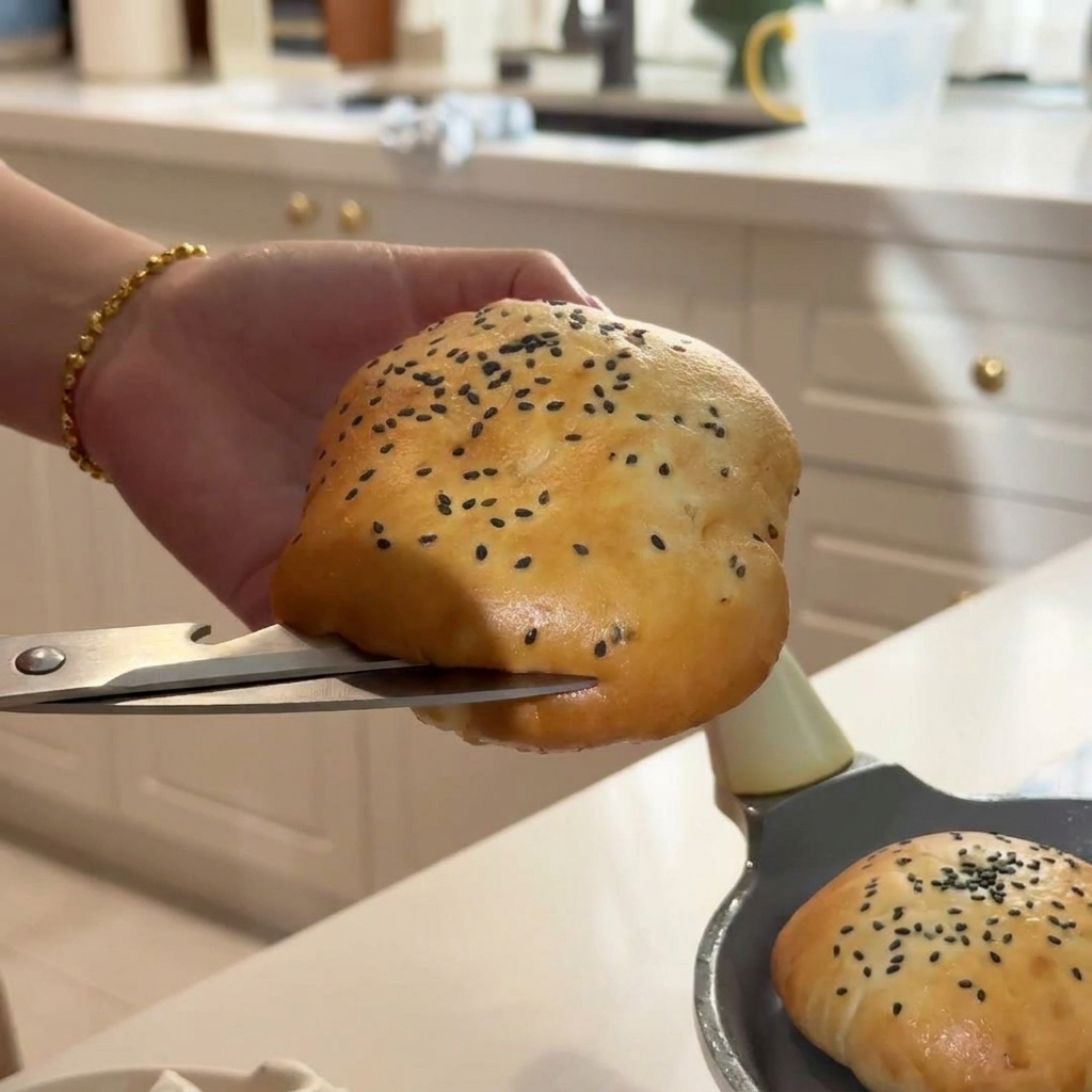 Une main coupant soigneusement un pain au sésame chaud à laide de ciseaux de cuisine argentés.