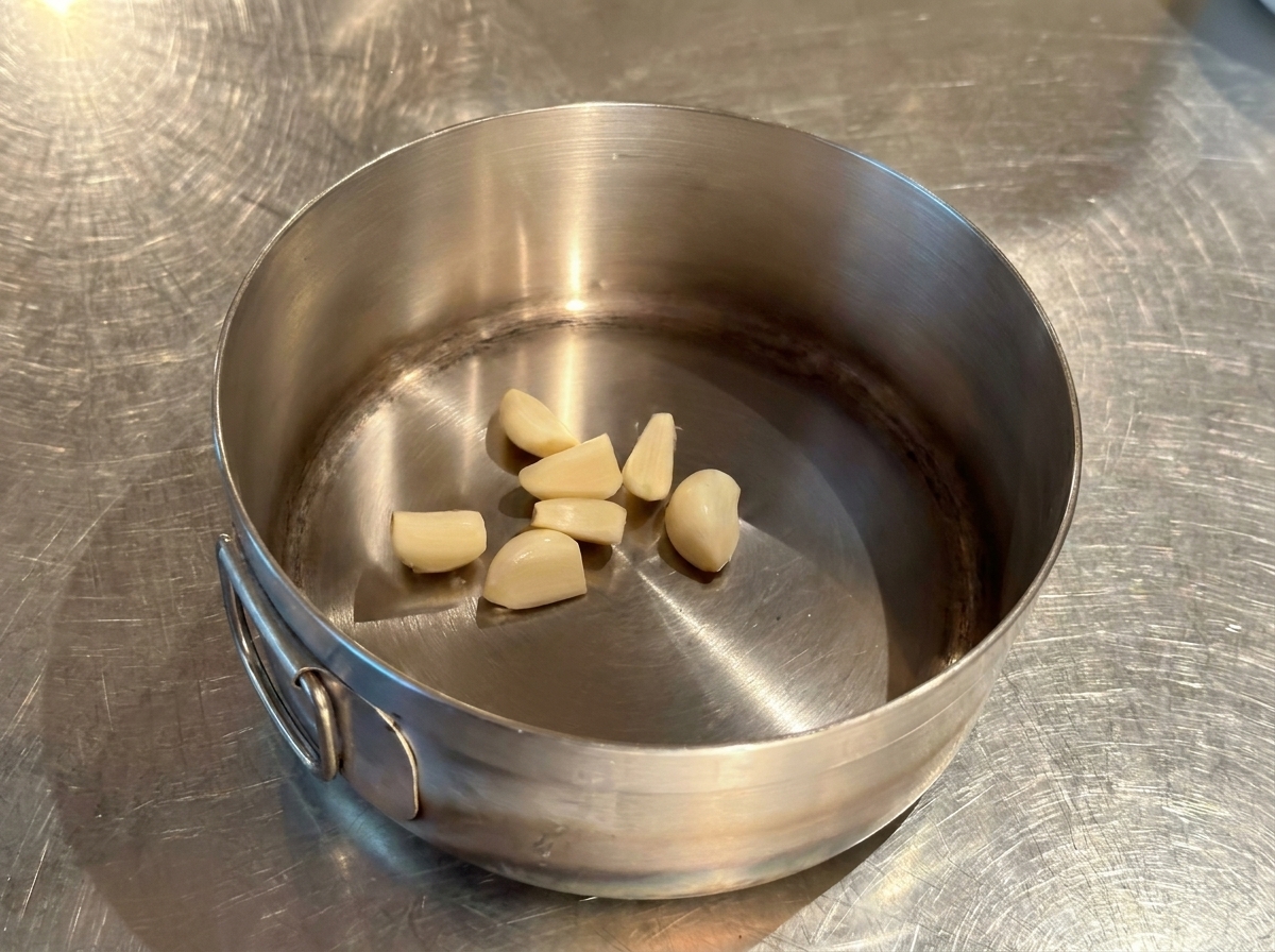 Gousses dail entières pelées reposant au fond dune petite casserole en inox bien sèche.