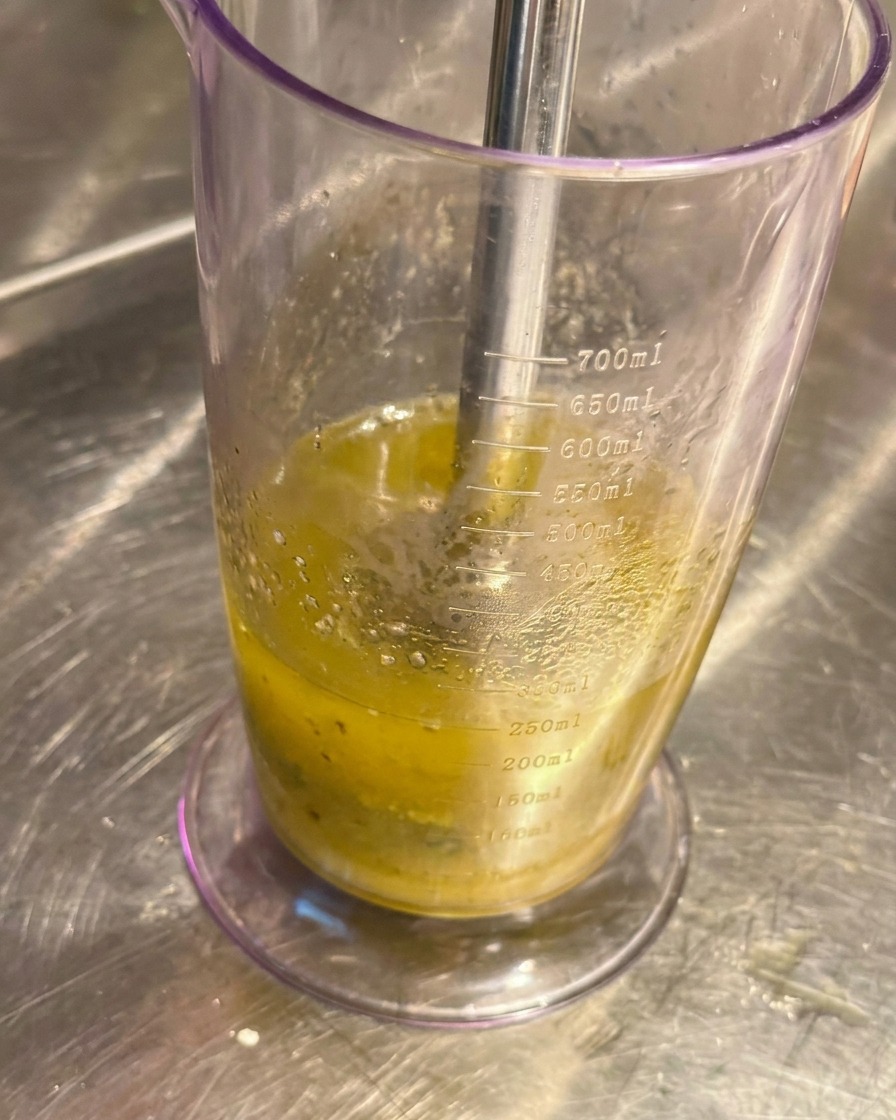 Mixeur plongeant dans un bécher transparent transformant lail confit et lhuile en une émulsion lisse.