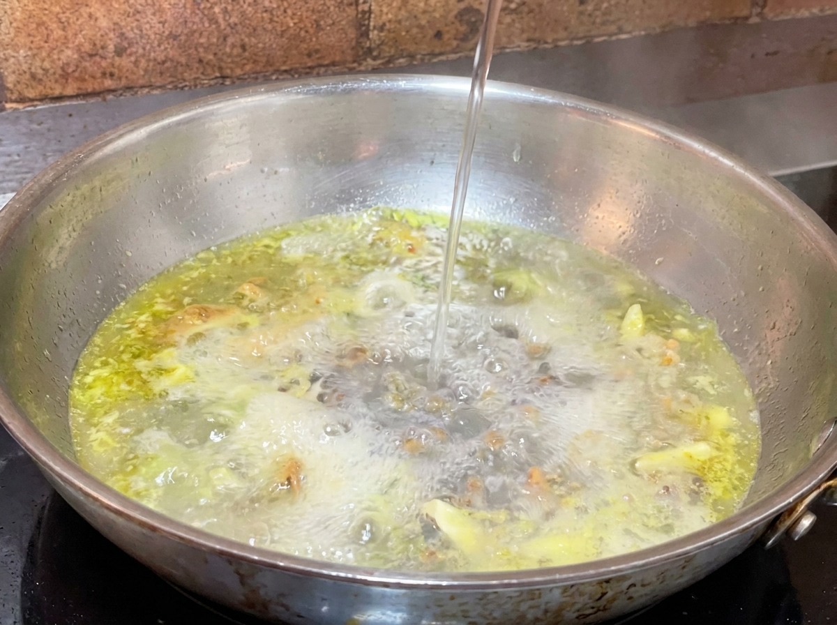 Louche deau de cuisson des pâtes versée dans la poêle dhuile et dail bouillante.