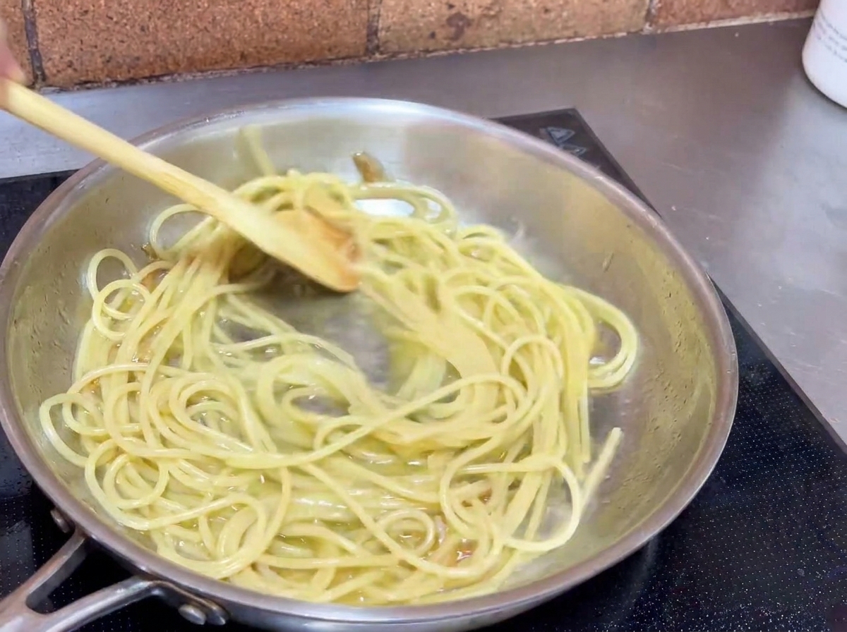Spaghetti mélangés dans la poêle avec une cuillère en bois pour bien les napper de sauce à lail.