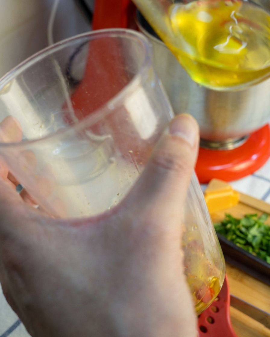 Un mixeur plongeant soulevé dun gobelet transparent, dégoulinant dune sauce lisse, rouge doré, mixée à lail et au piment.