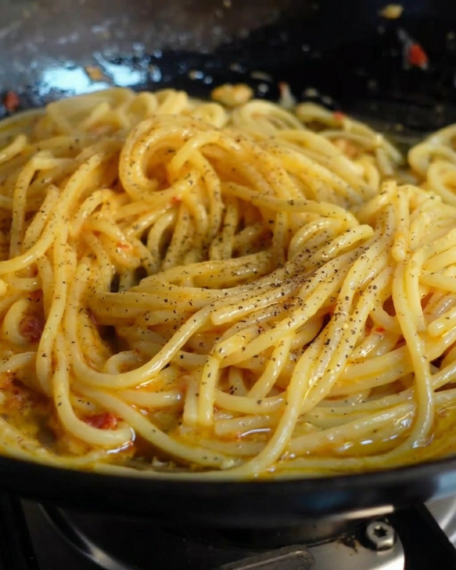 Du poivre noir fraîchement moulu parsemé sur une poêle de spaghettis luisants.