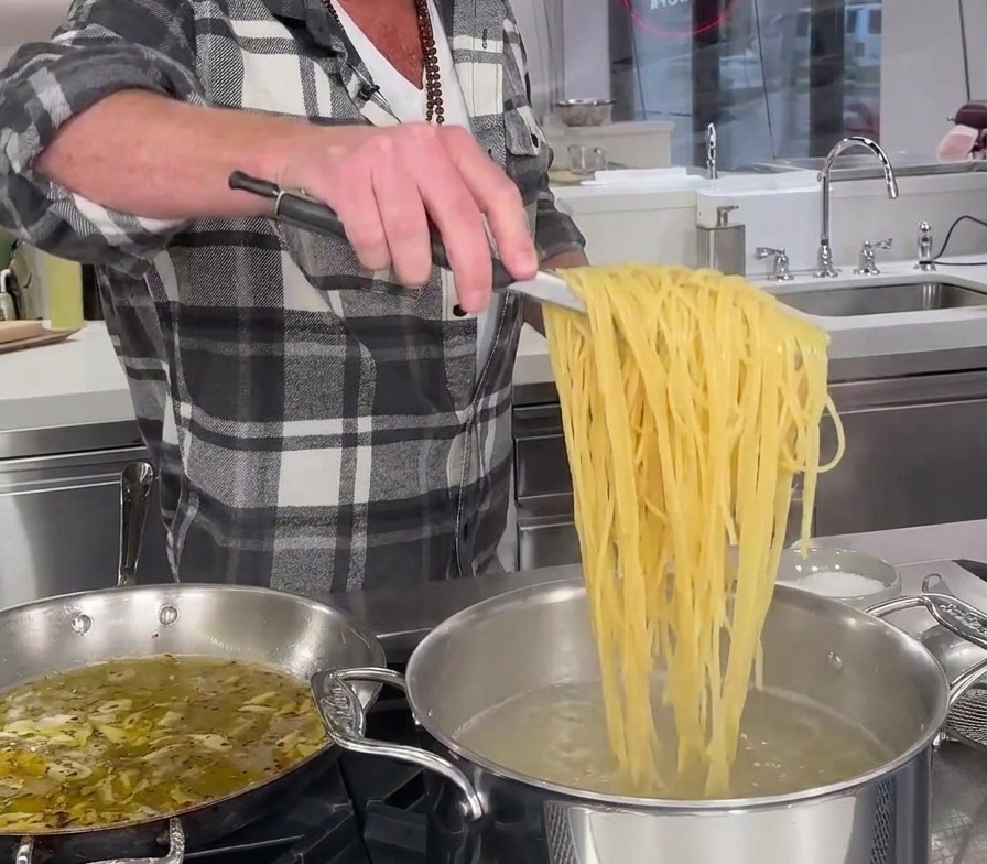 Spaghetti partiellement cuits soulevés directement dune marmite deau bouillante avec des pinces métalliques.