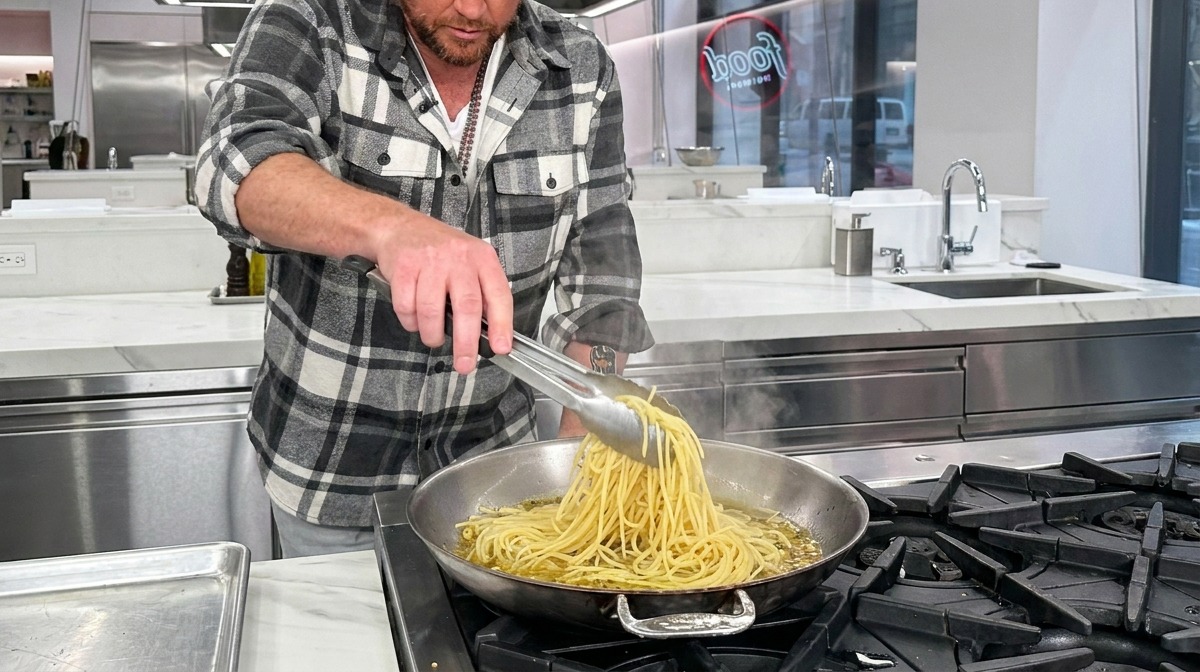 Spaghetti mi-cuits déposés dans une poêle chaude avec ail, huile et eau de cuisson à laide de pinces.