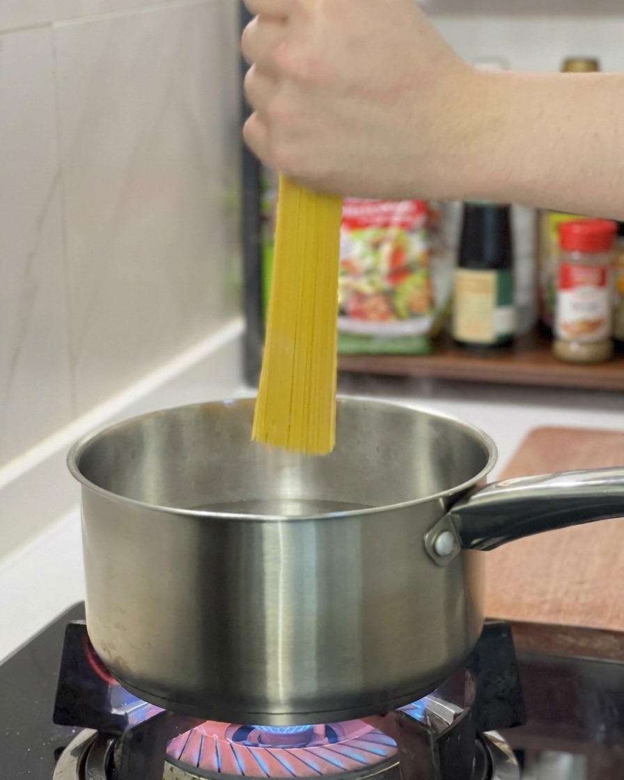 Une main plongeant un faisceau de spaghetti secs dans une casserole en inox remplie deau bouillante.