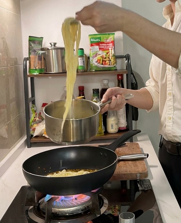 Longs brins de spaghetti cuits soulevés dune casserole avec une pince pour être ajoutés dans une poêle chaude contenant lhuile parfumée.