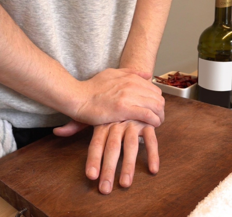 Mains pressant fermement pour écraser des gousses dail frais sur une planche à découper en bois.