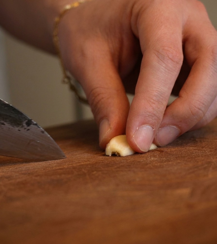 Gros plan de doigts tenant un morceau dail pendant quun couteau de chef le hache finement.