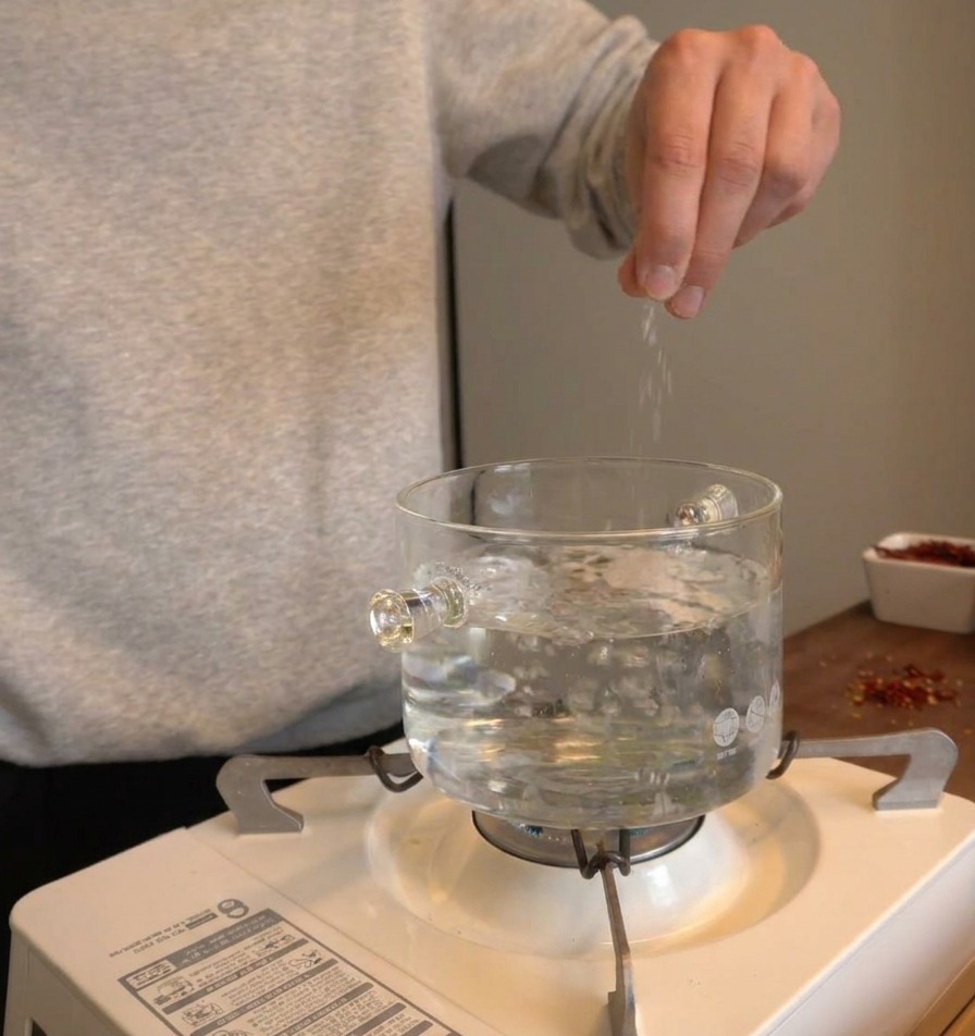 Une main saupoudrant du sel dans une casserole deau bouillante sur un réchaud.