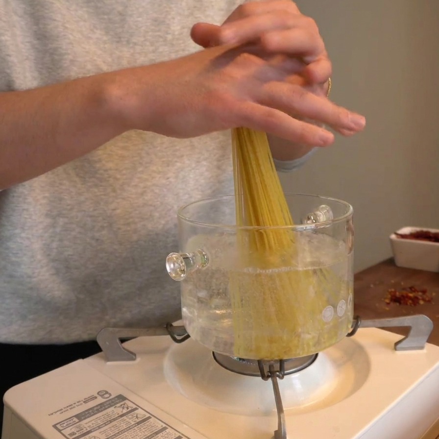 Mains déposant un bouquet de spaghetti secs verticalement dans une casserole deau bouillante.