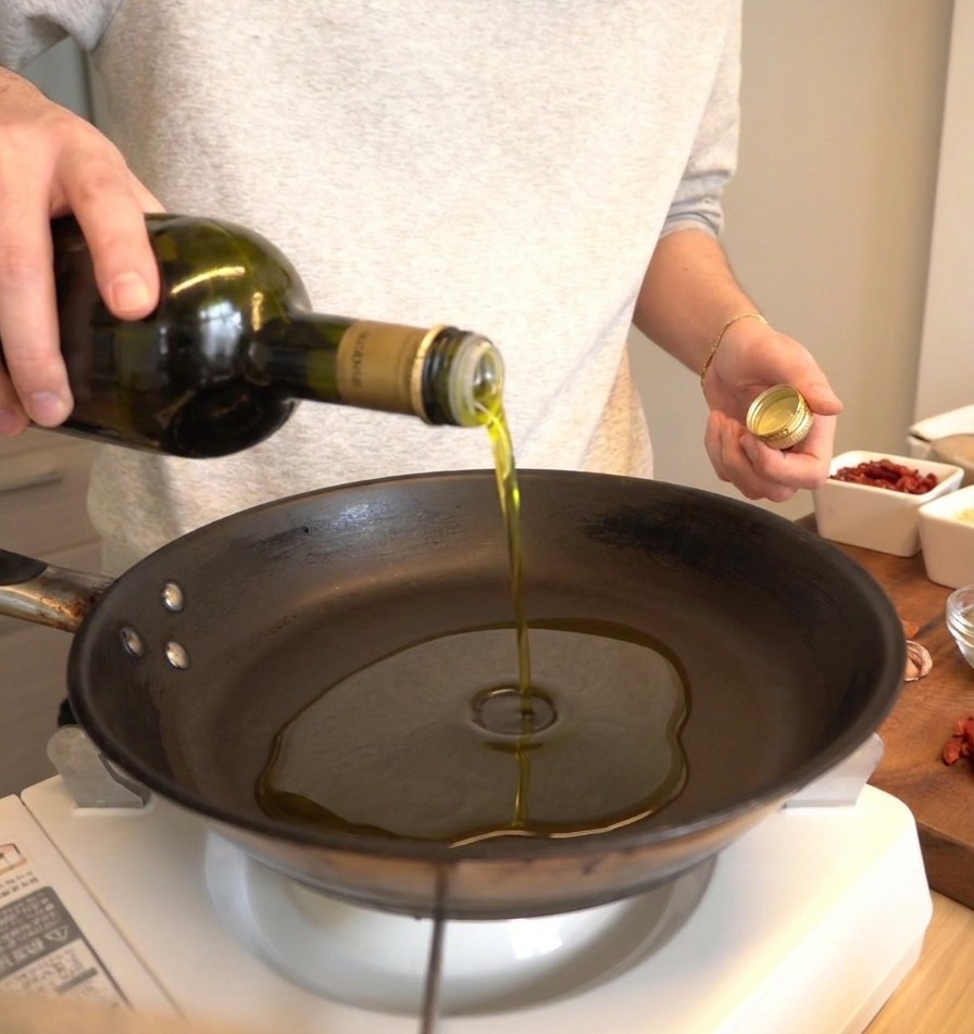 Huile dolive versée dune bouteille en verre foncé dans une poêle noire.
