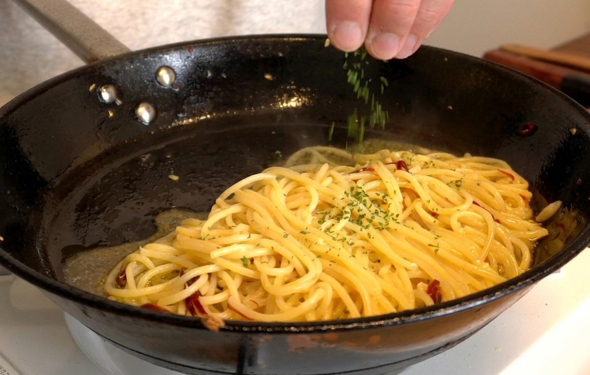Une main saupoudrant du persil vert frais haché sur une poêle de spaghetti brillants.