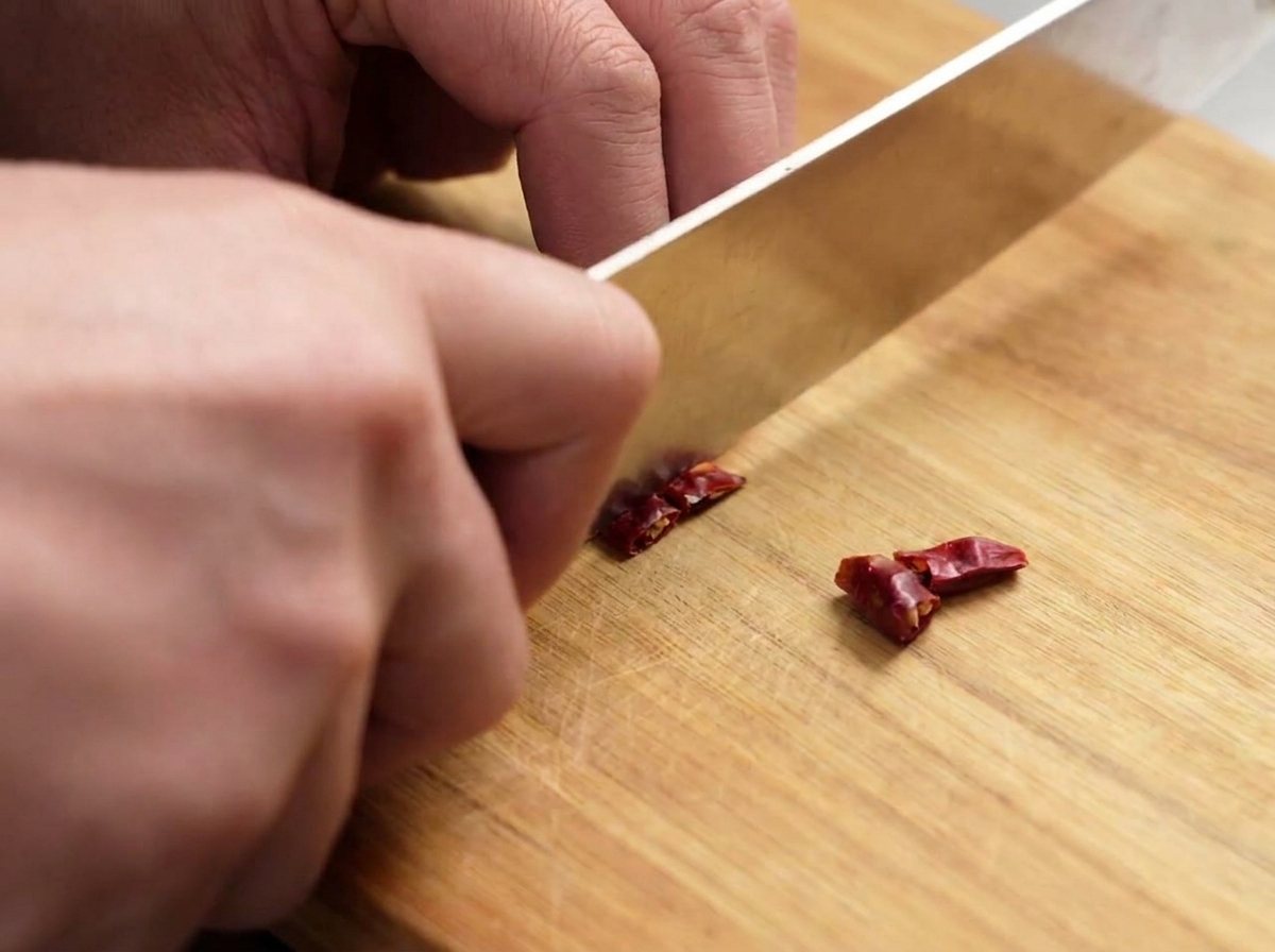 Couteau découpant des piments rouges séchés en petits morceaux sur une planche à découper.
