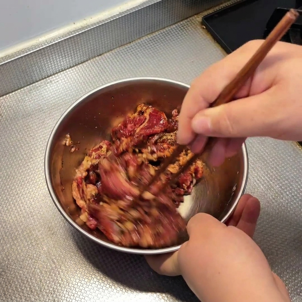 Utilisation de baguettes en bois pour mélanger rapidement le bœuf cru dans un bol en métal.