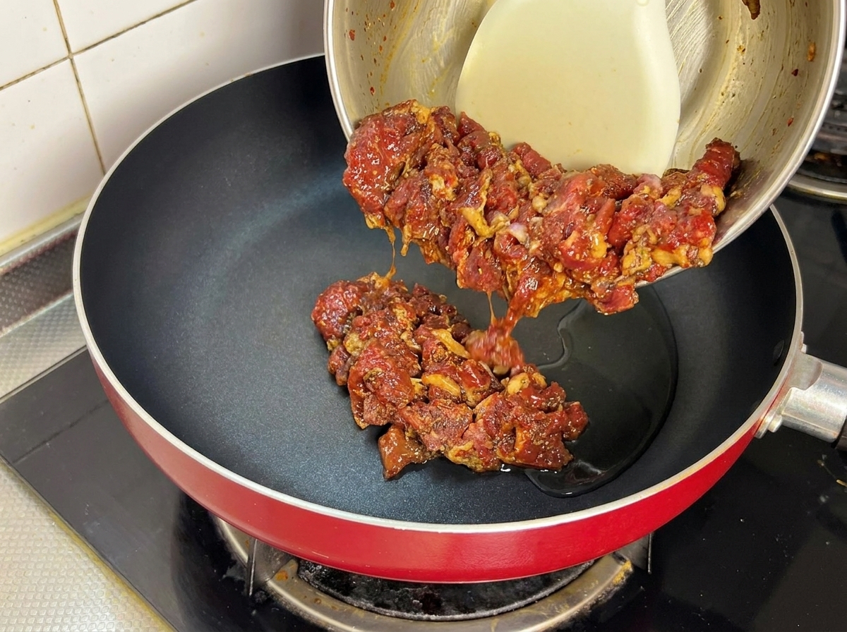 Bœuf mariné cru versé dun bol dans une poêle chaude avec de lhuile.