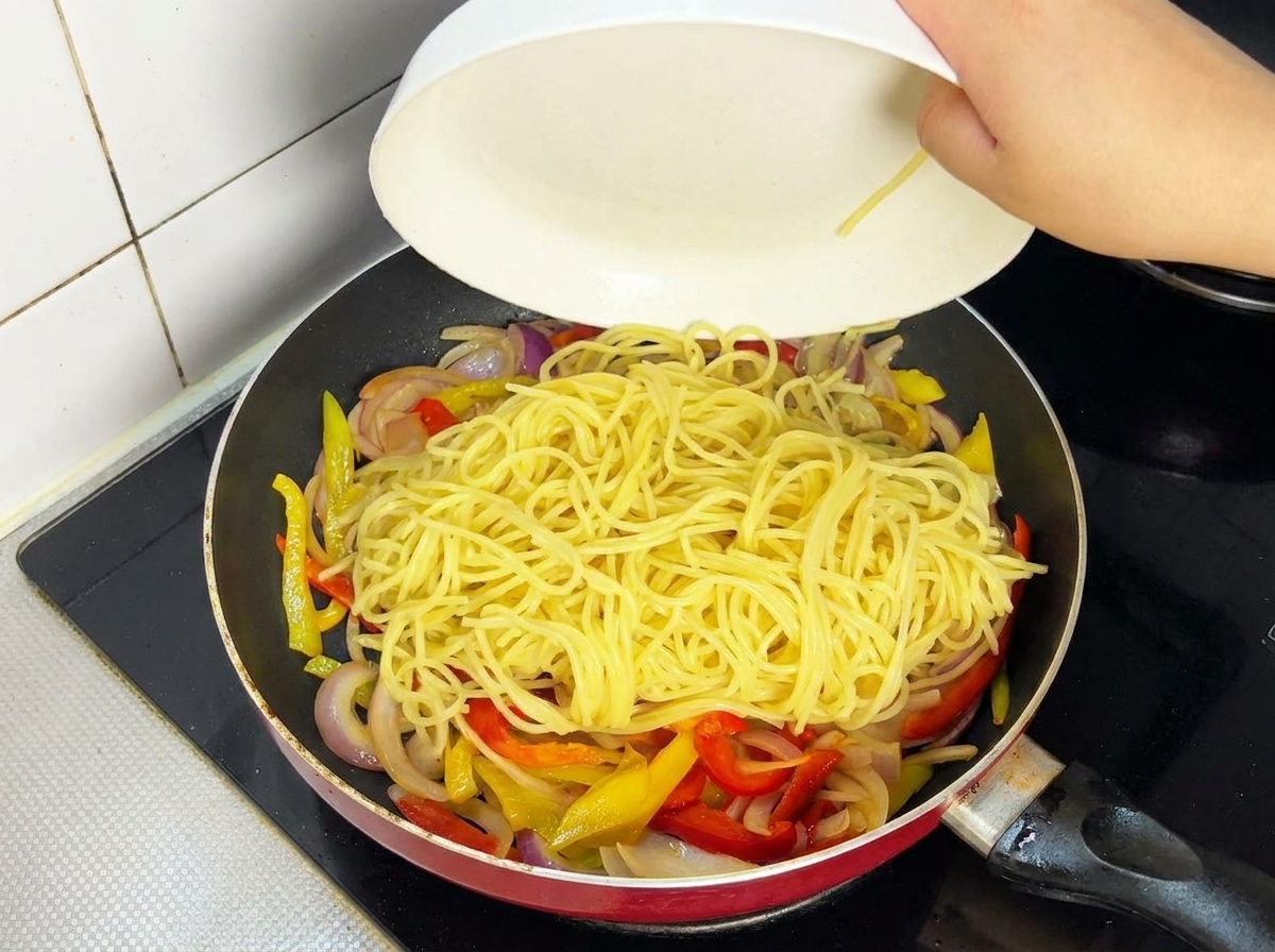 Tranches de bœuf cuites rajoutées dans une poêle contenant les spaghetti et les légumes.