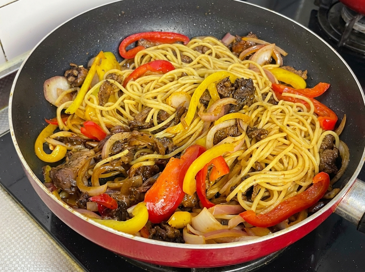 Spaghetti au poivre noir, bœuf et poivrons bien mélangés et nappés de sauce brillante dans une poêle.
