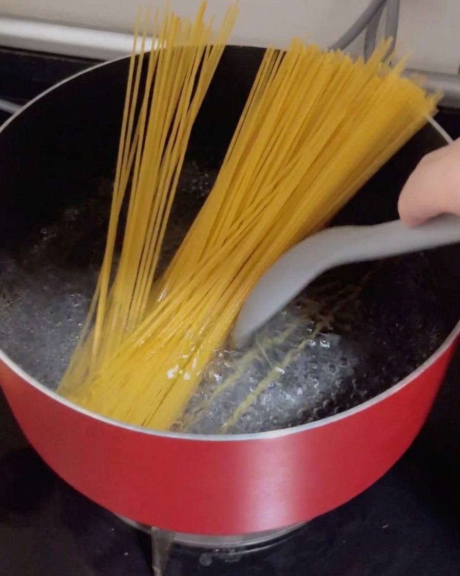 Des spaghetti secs plongés dans une casserole rouge deau bouillante.