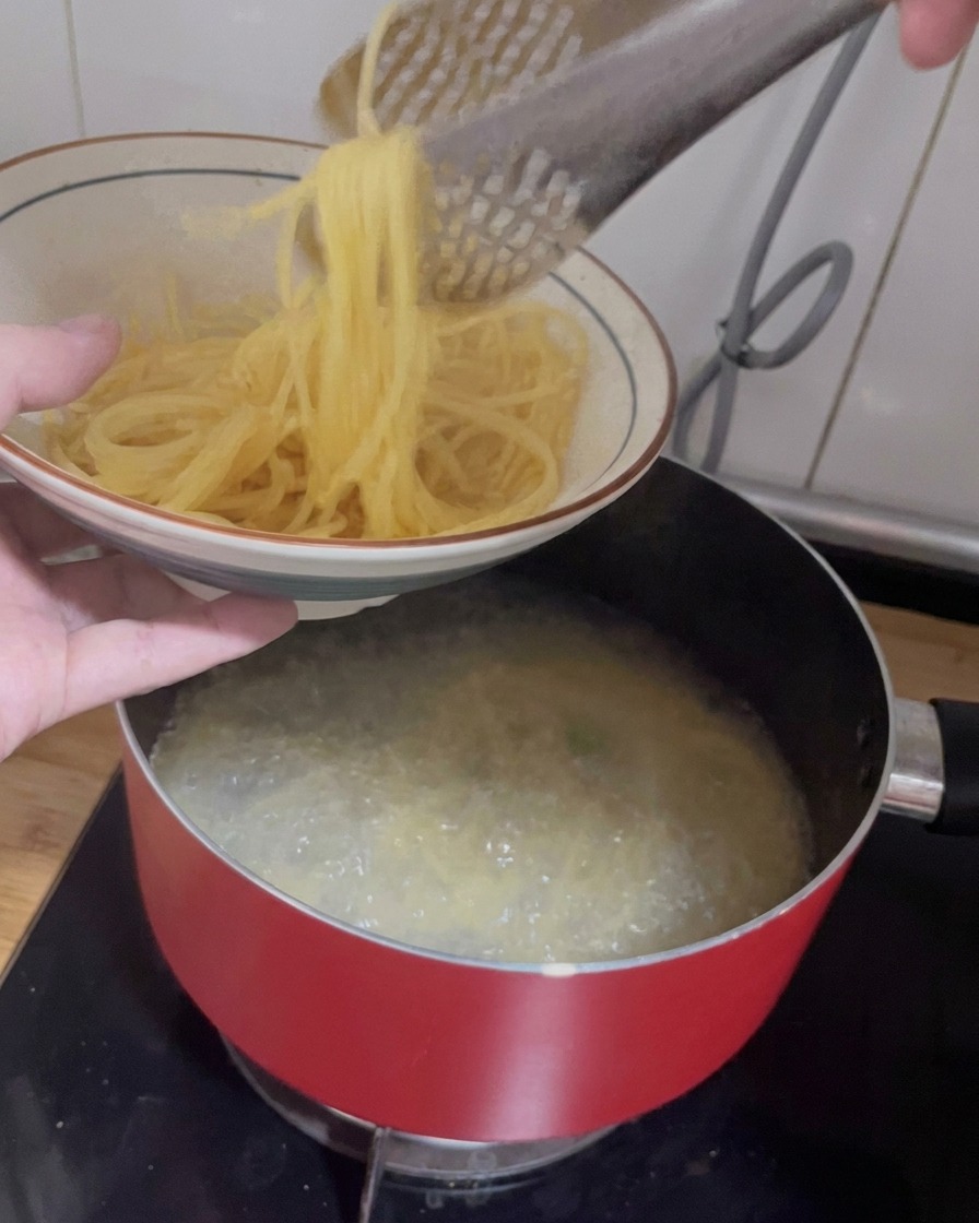 Une pince soulevant des spaghetti cuits dune casserole pour les déposer dans un bol en céramique décoré.