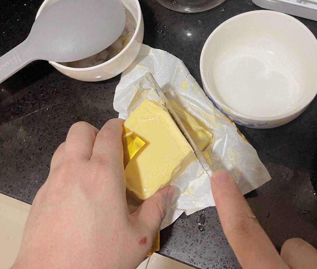 Une personne coupant une tranche épaisse dans un bloc de beurre jaune avec un grand couteau de cuisine.