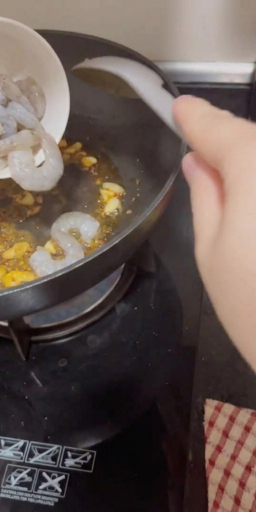 Des crevettes crues et décortiquées versées dun bol dans la poêle chaude avec lail et le piment.