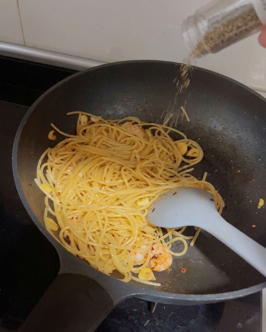 Un moulin distribuant du poivre noir frais sur la poêle de spaghetti et de crevettes.