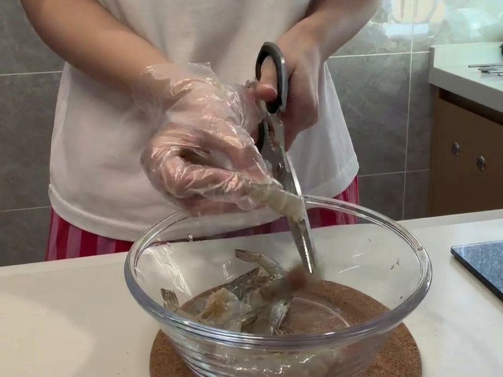 Une personne portant des gants utilise des ciseaux pour couper soigneusement le dos dune crevette crue.