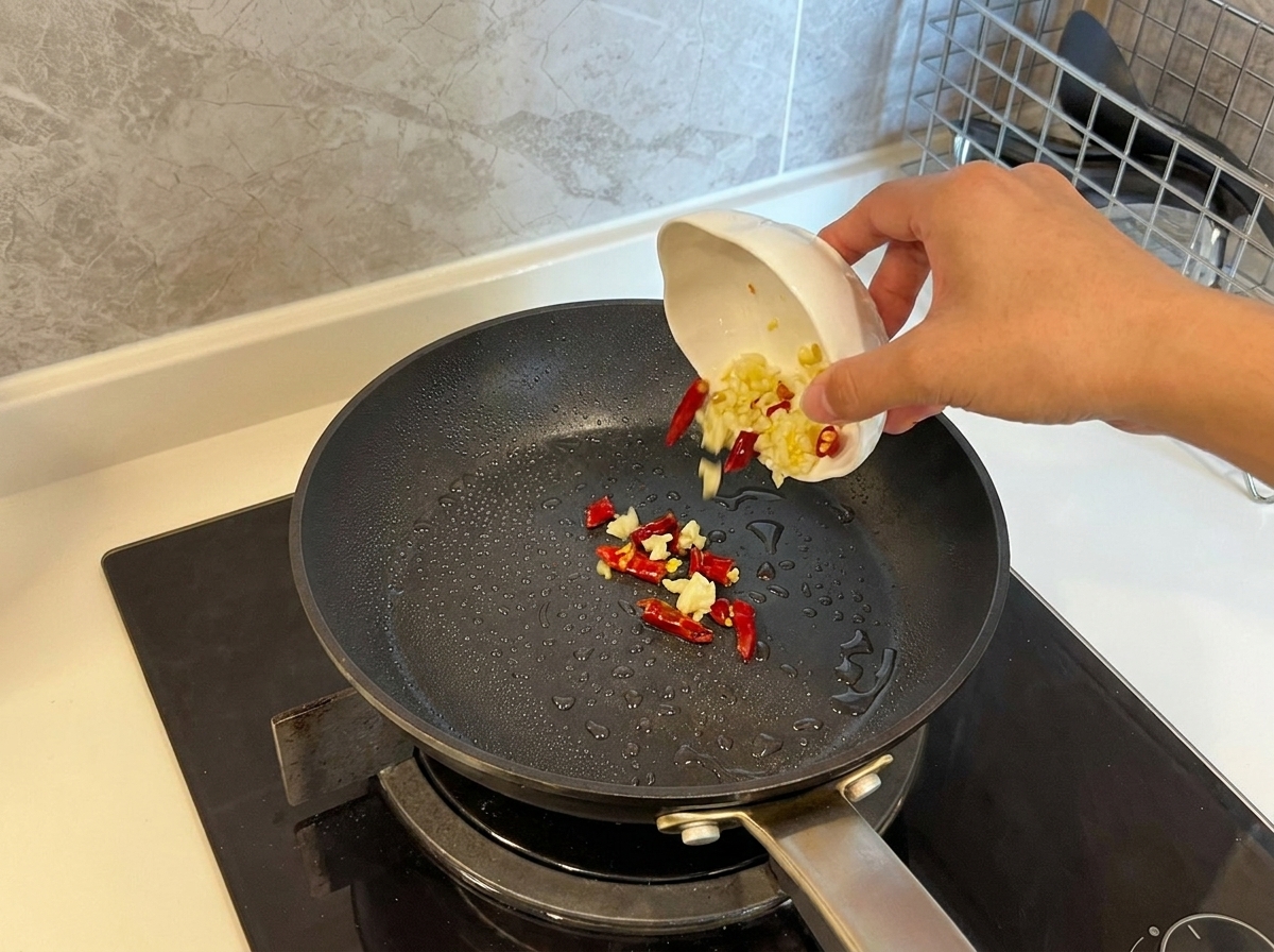 De lail émincé et des piments rouges séchés versés dun petit bol dans une poêle chaude et huilée.
