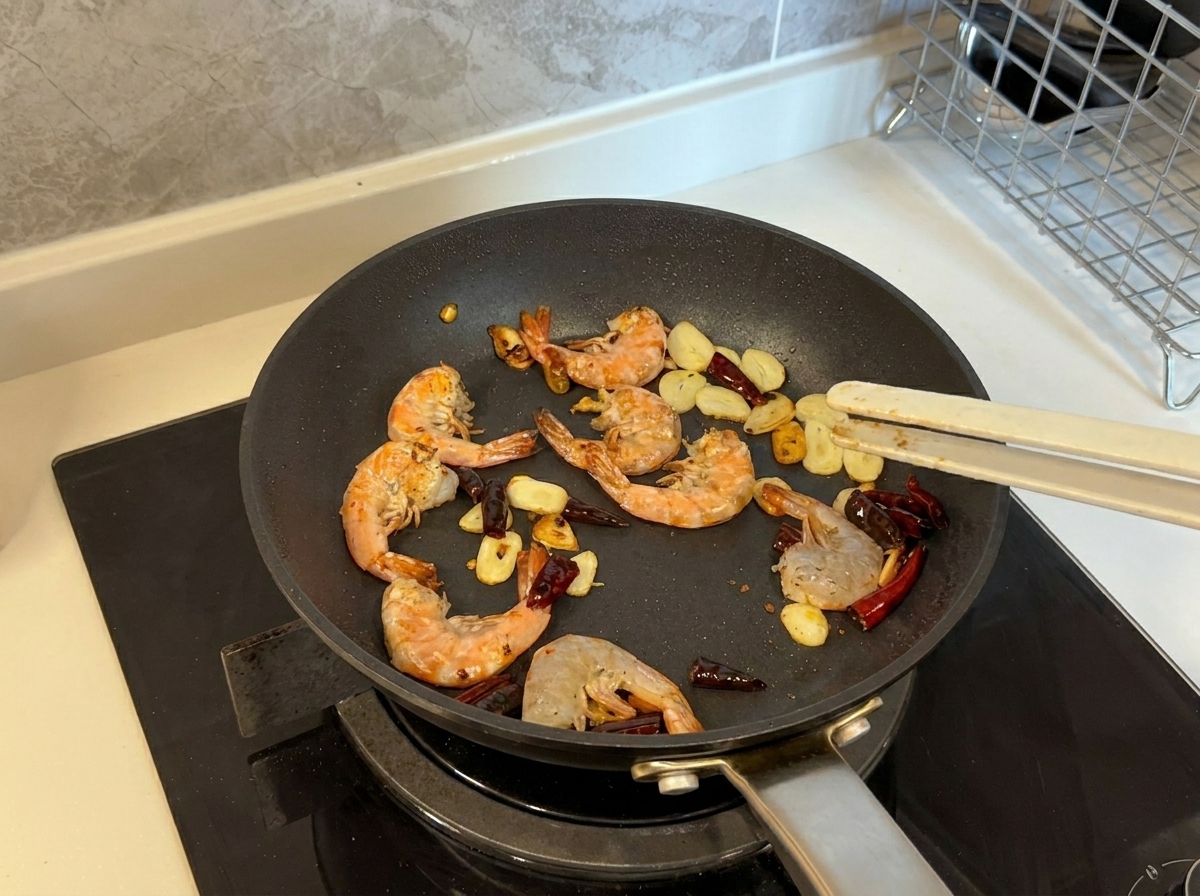 Des crevettes devenant roses et dorées alors quelles sont sautées avec de lail et des piments dans une poêle.