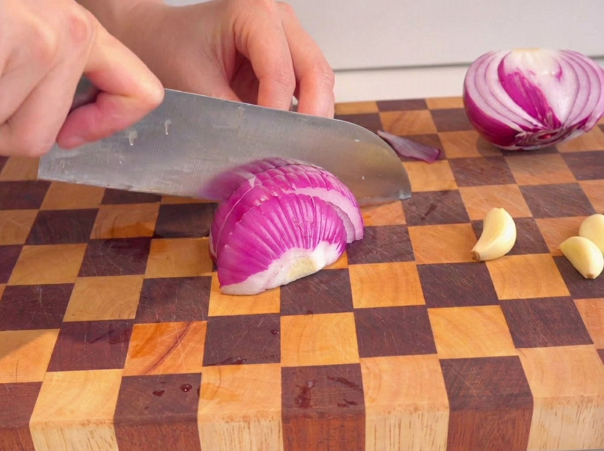 Mains utilisant un couteau pour hacher un oignon rouge sur une planche à découper.