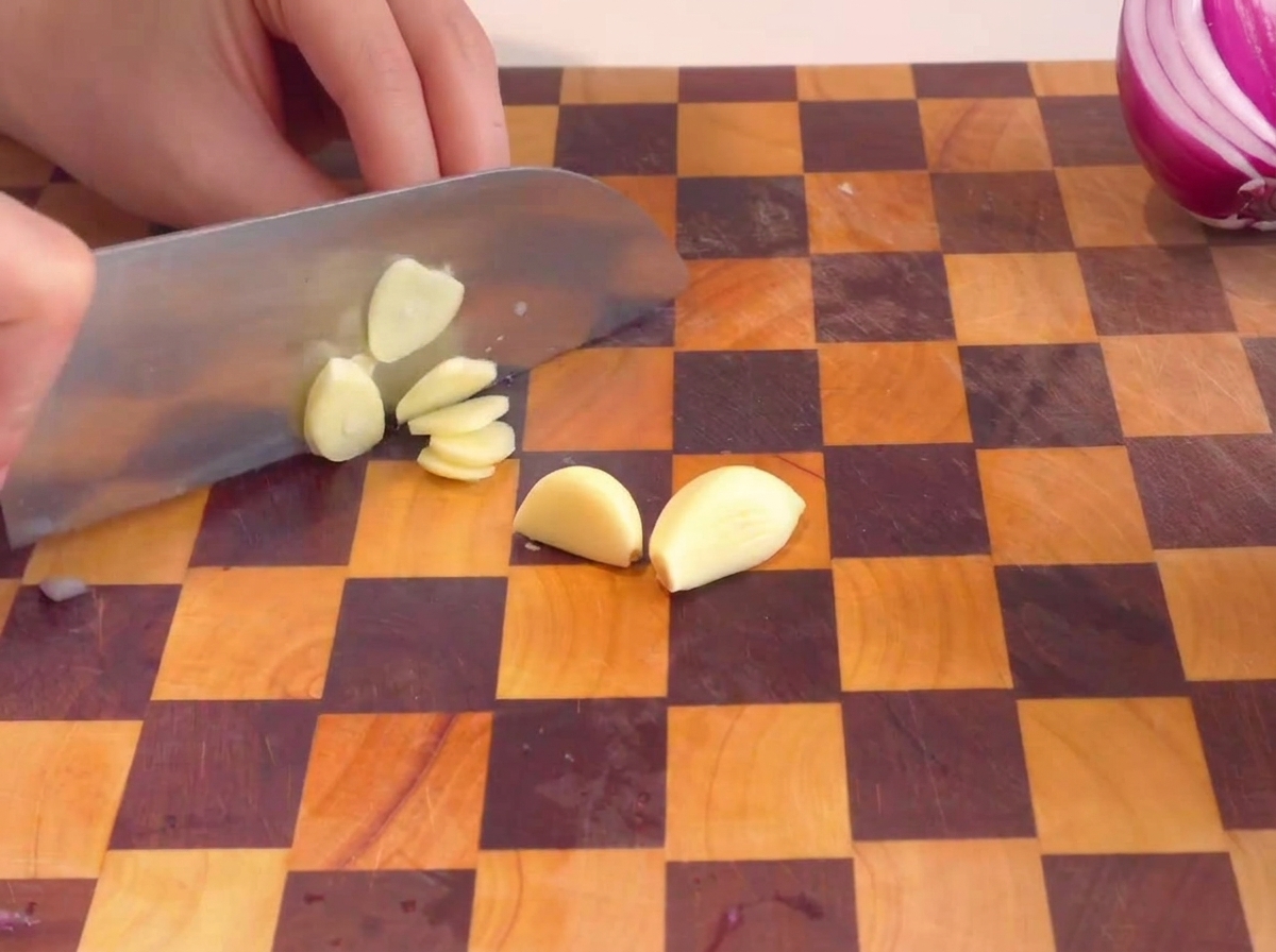 Mains tranchant des gousses dail épluchées sur une planche à découper en bois.