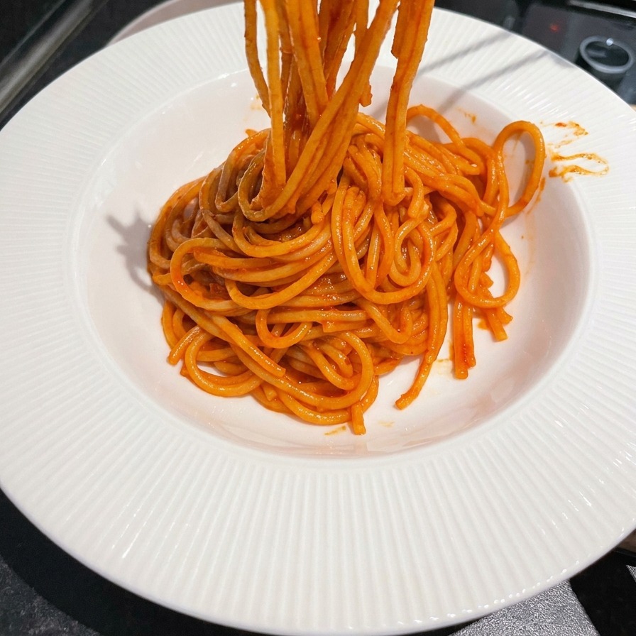 Baguettes en métal enroulant des spaghetti rouges brillants dans un bol de service blanc.