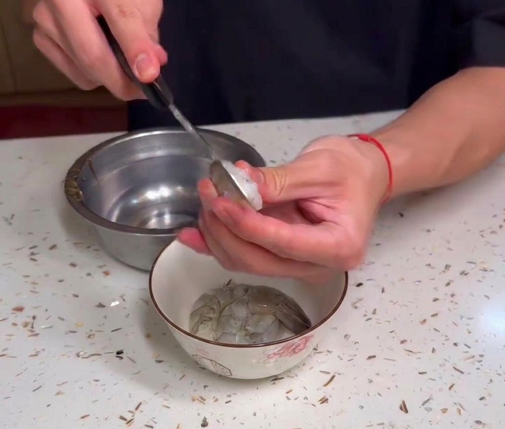 Mains nettoyant des crevettes crues au-dessus dun bol posé sur un plan de travail moucheté.
