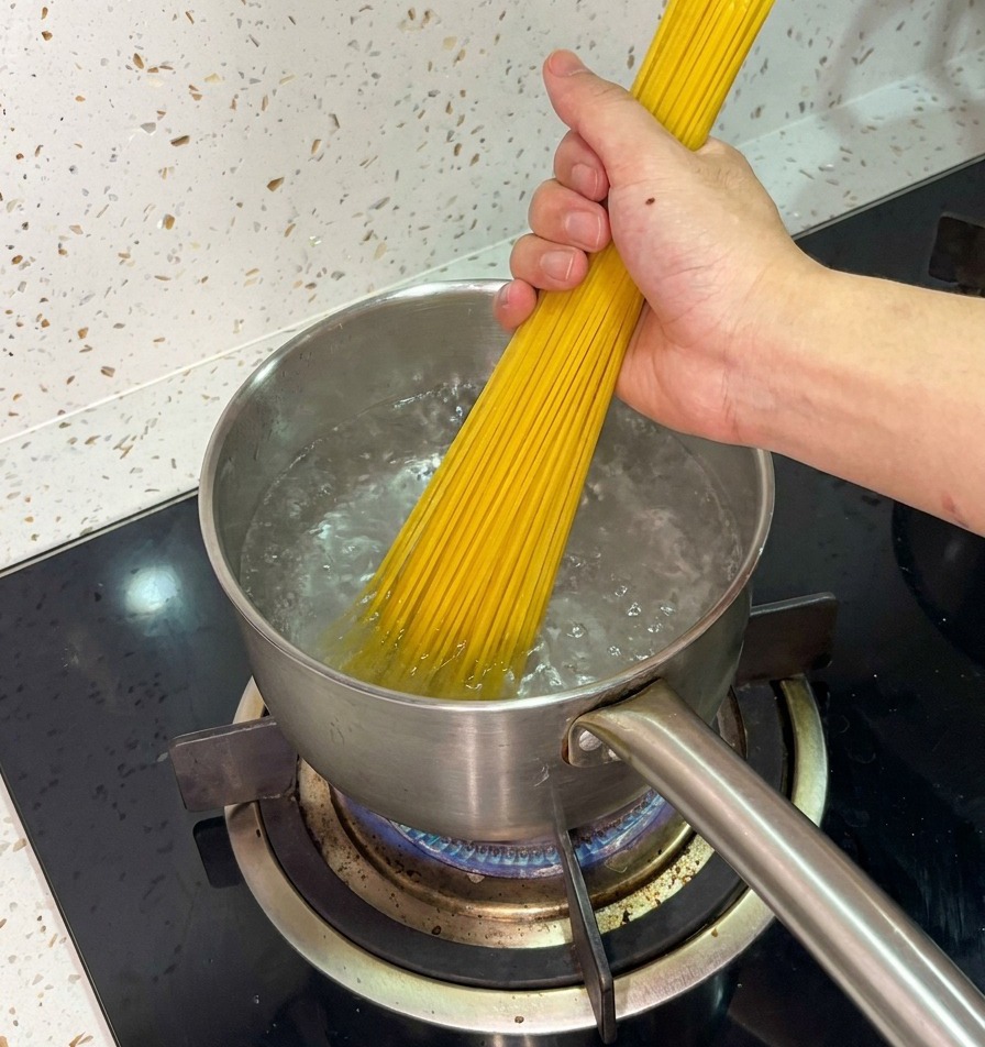 Une main tenant fermement un faisceau de spaghettis secs et les plongeant dans une casserole deau bouillante.