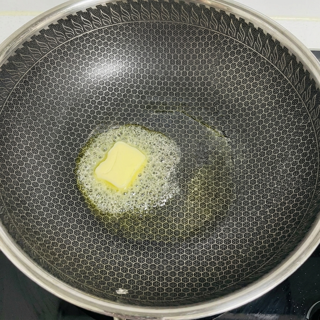 Un morceau de beurre blond fondant et moussant au centre dun grand wok noir à motif alvéolé.