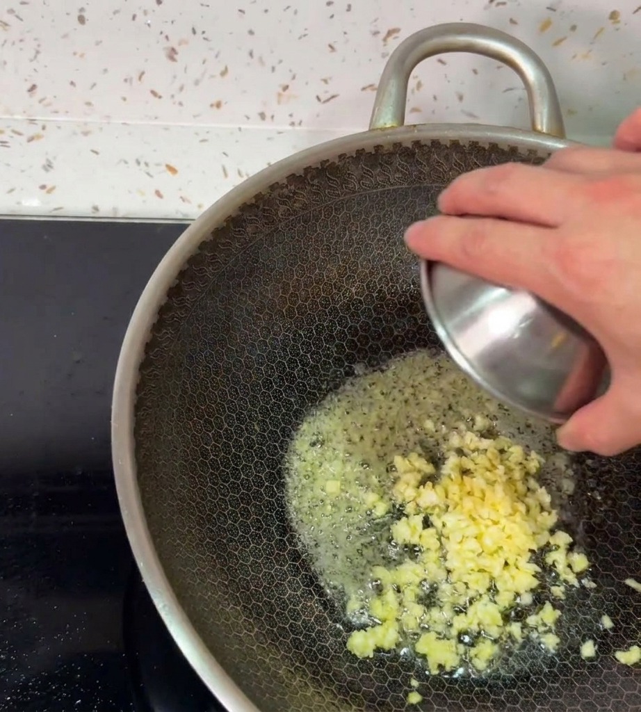 Une main versant de lail fraîchement haché dans le beurre moussant à lintérieur dun wok chaud.