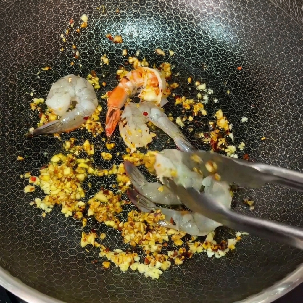 Utilisation dune pince pour déposer des crevettes crues dans un wok rempli de beurre à lail et au piment.